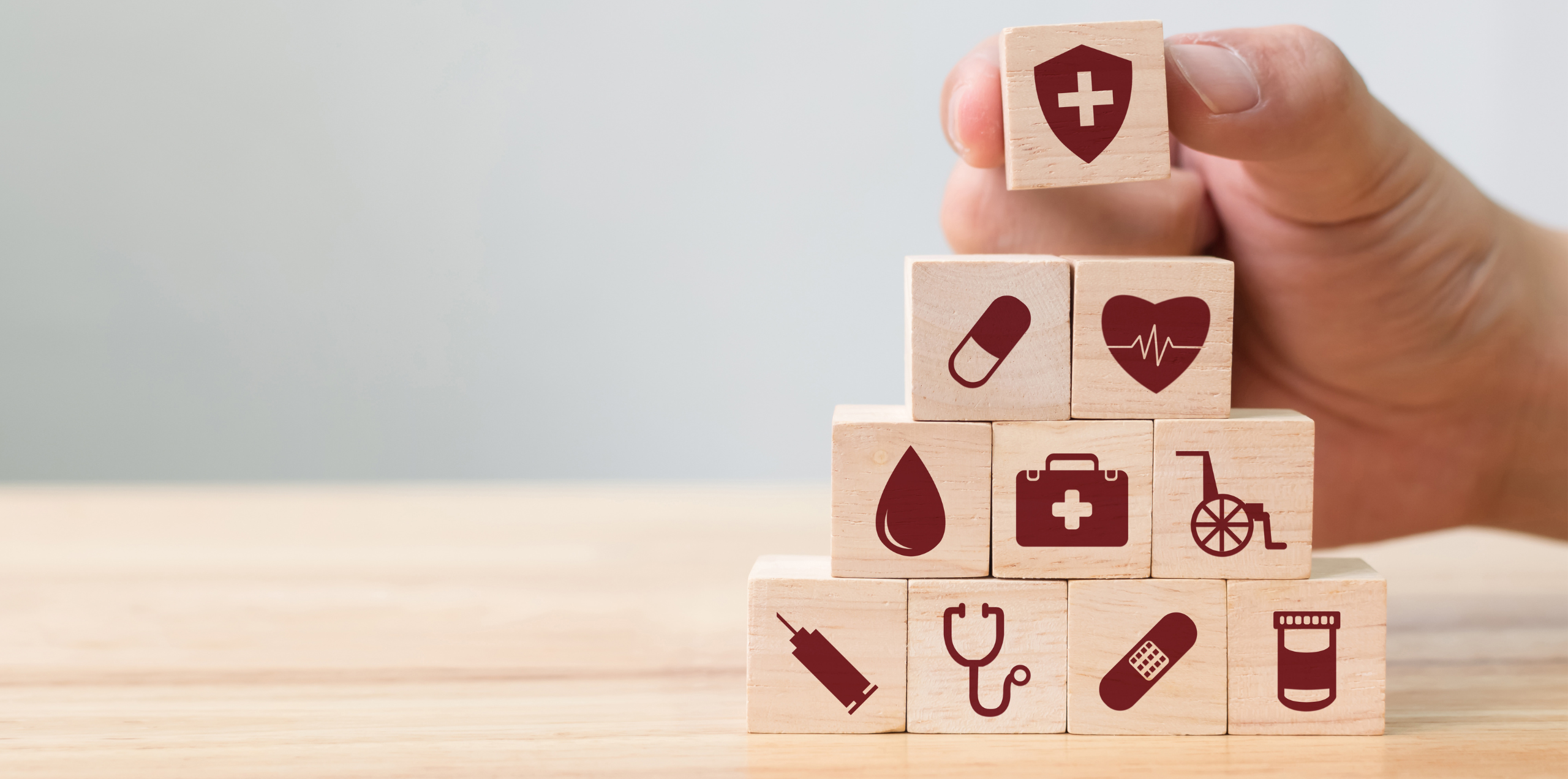 A hand places a final wooden block atop a pyramid of blocks depicting various icons of health and medicine.